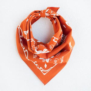 Burnt orange bandana with white screen print. Shown bandit style. Nouveau, stylized grape motif with leaves.