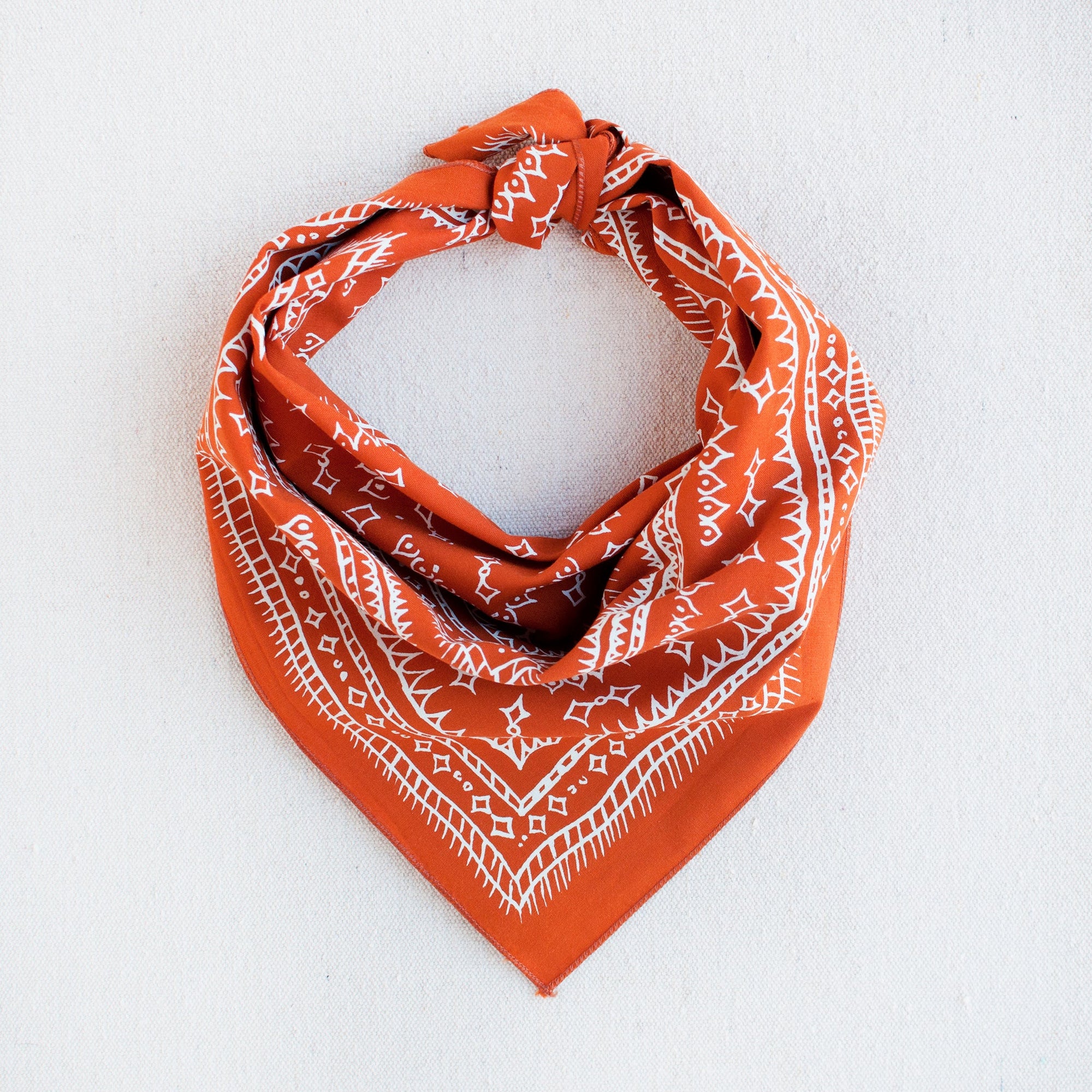 Marmalade orange and white hand drawn diamond printed bandana, styled in a triangle, bandit style. 