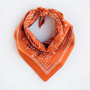 Orange and white bandana with geometric pattern of dots and dashes. Styled in a triangle neck scarf or bandit style.