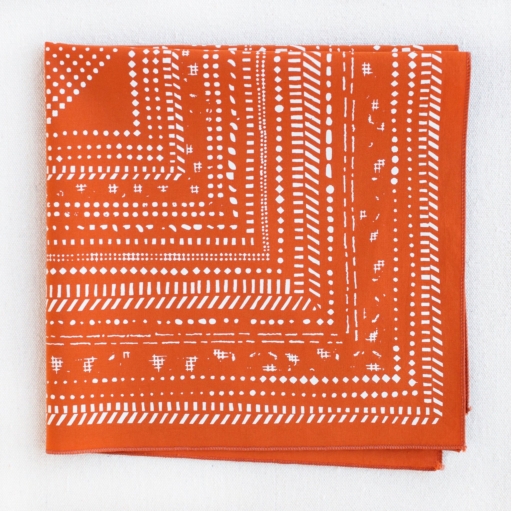 Graphic burnt orange and white halftone geometric pattern bandana. Folded into quarters.