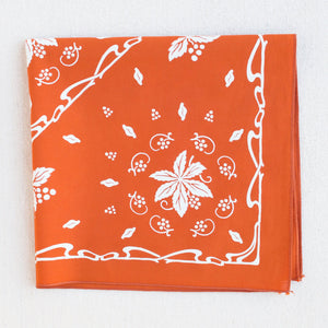 Burnt orange bandana with white screen print. Shown folded in quarters. Nouveau, stylized grape motif with leaves.