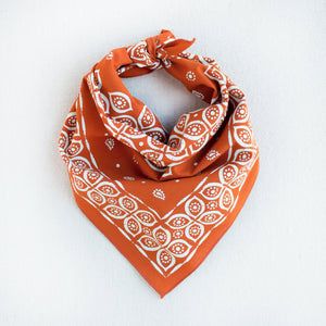 Marmalade orange bandana with stylized eye and paisley print. Styled as a triangle scarf.
