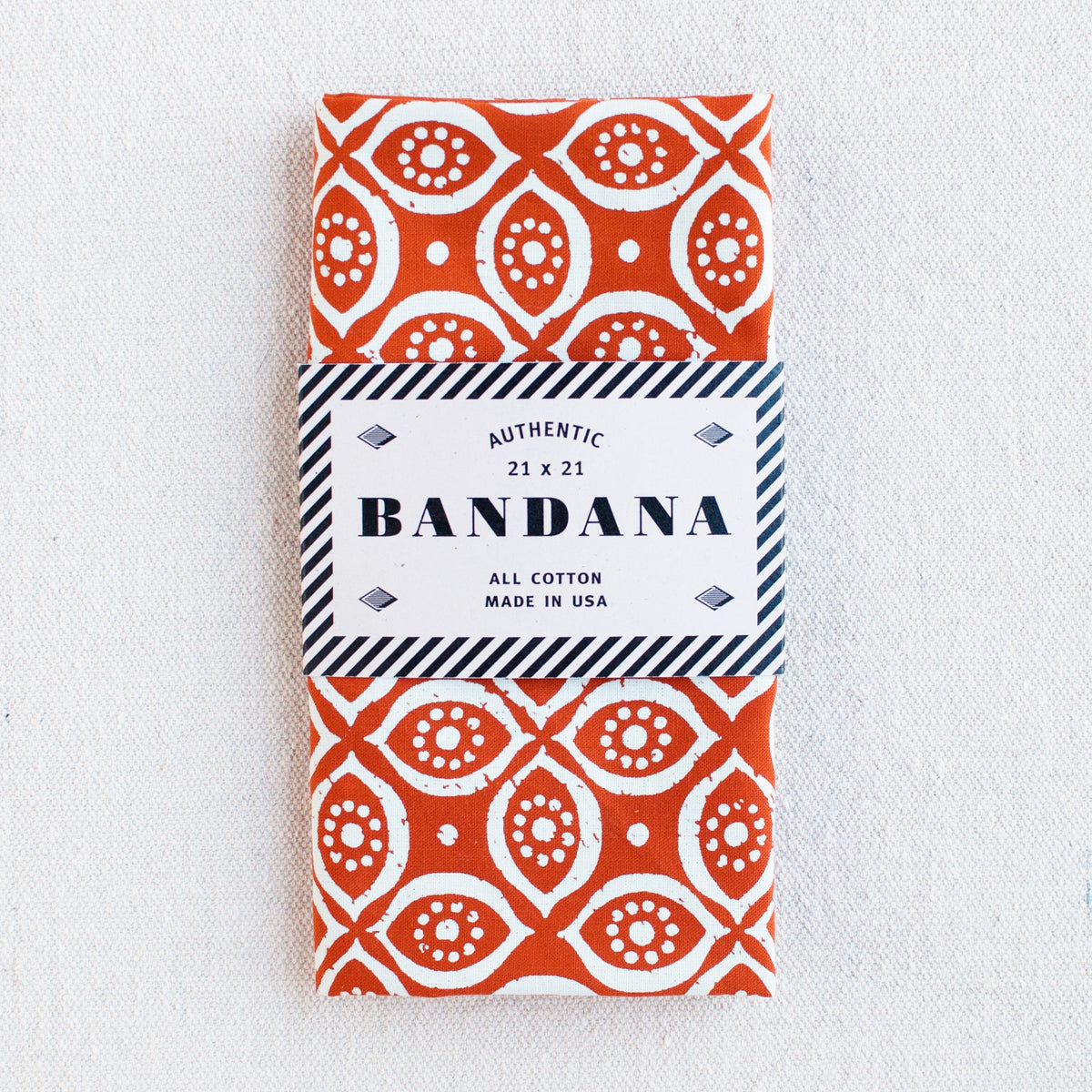 Burnt orange bandana with white screen print. Vintage stylized eye print, folded and packaged in eco-friendly recycled paper band.