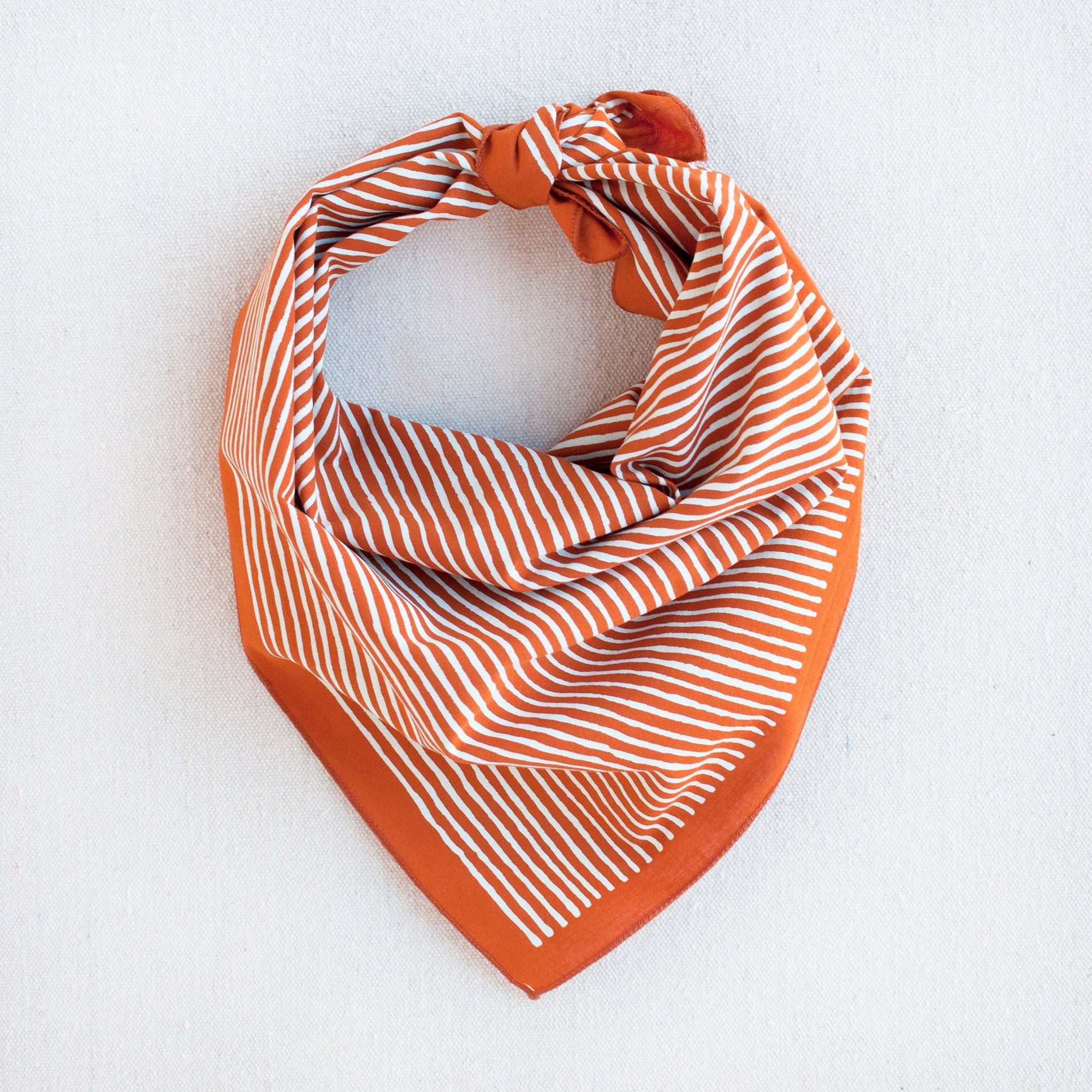 Burnt orange bandana with white striped screen print, styled as a triangle scarf.